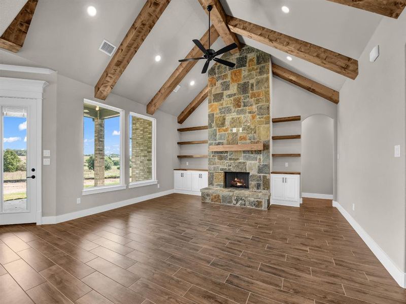 Unfurnished living room featuring a fireplace, high vaulted ceiling, wood finish floors, beamed ceiling, and a ceiling fan