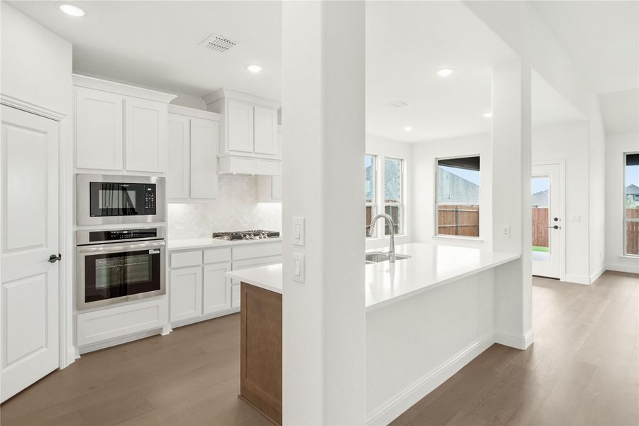 Kitchen with white cabinets, stainless steel appliances, large island with sink, and hardwood floors Kitchen with white cabinets, stainless steel appliances, large island with sink, and hardwood floors