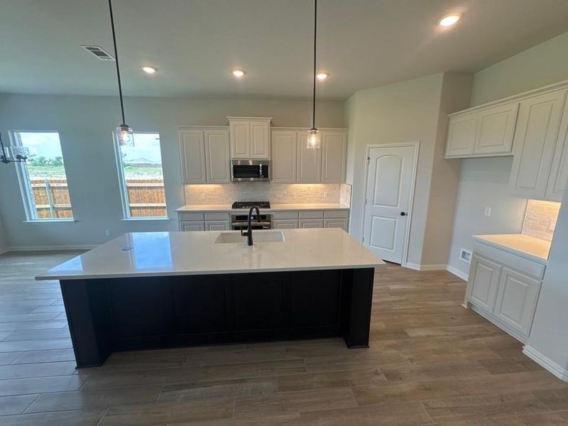 Modern kitchen featuring a large island with an integrated sink, light-toned cabinetry, stainless steel appliances, tile backsplash, and recessed lighting