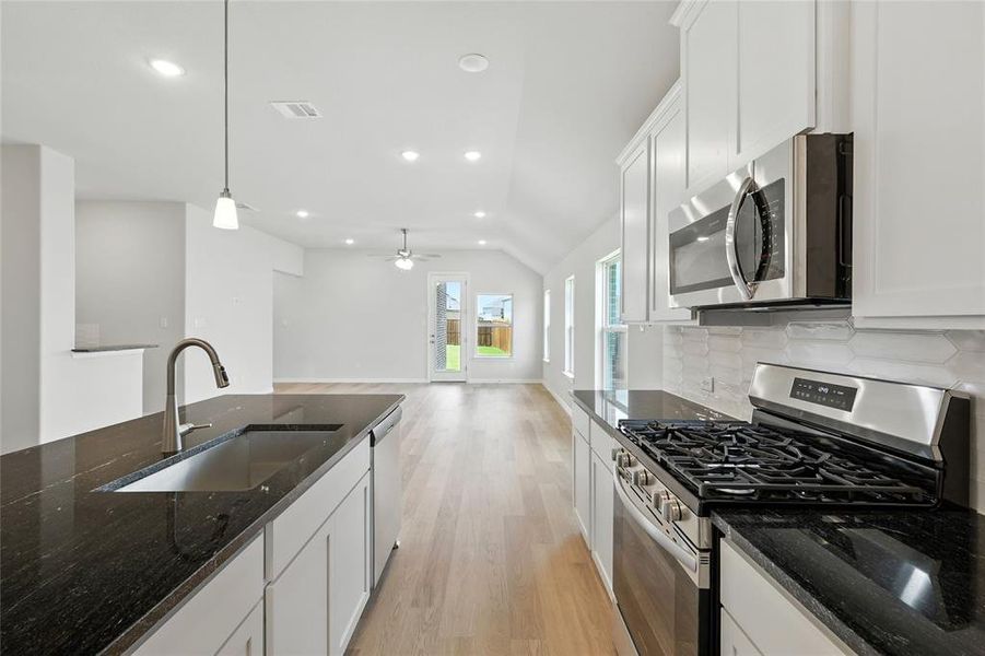 Kitchen featuring stainless steel appliances, white cabinets, dark stone counters, and vaulted ceiling