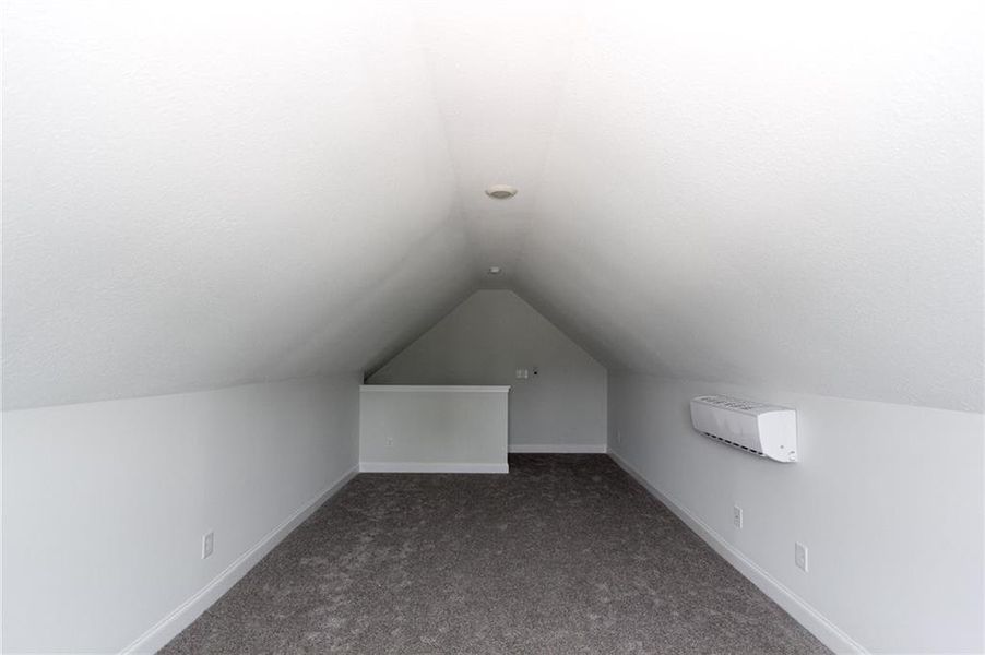 Additional living space with dark colored carpet and vaulted ceiling