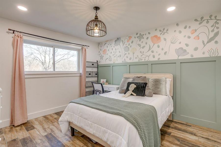 Bedroom featuring wallpapered walls, a decorative wall, light wood-style floors, wainscoting, and suspended lighting