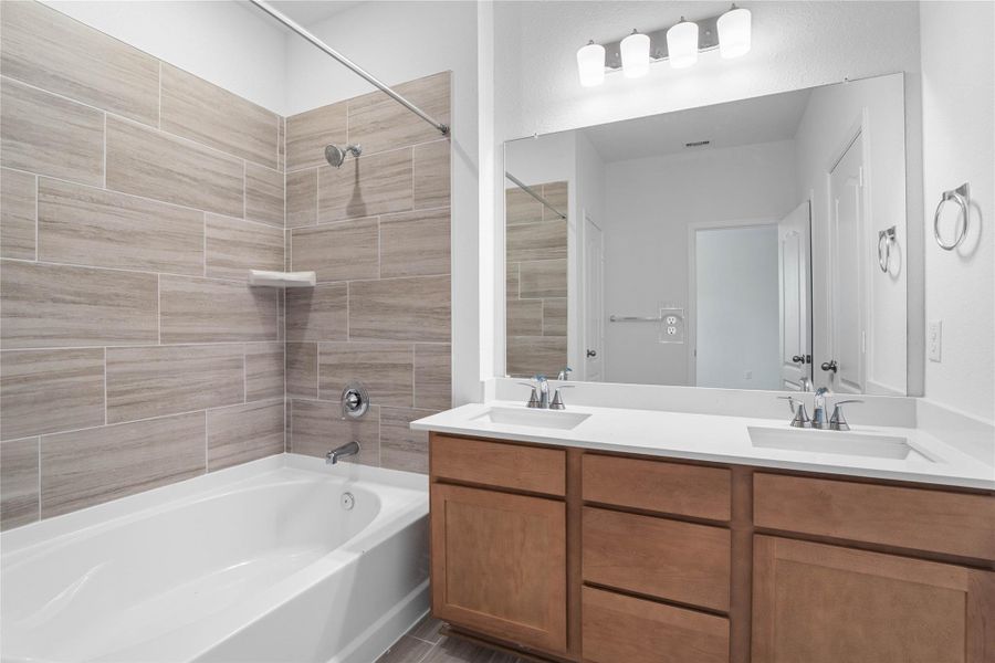 This move-in ready primary bathroom offers a spacious tub/shower combination with a tiled surround, stained cabinetry topped with light countertops, dual sinks, high ceilings, neutral paint, a large mirror, and sleek, modern finishes for a polished look. This move-in ready primary bathroom offers a spacious tub/shower combination with a tiled surround, stained cabinetry topped with light countertops, dual sinks, high ceilings, neutral paint, a large mirror, and sleek, modern finishes for a polished look.