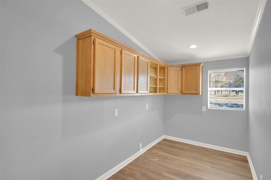 Empty room with crown molding, light wood-type flooring, and lofted ceiling