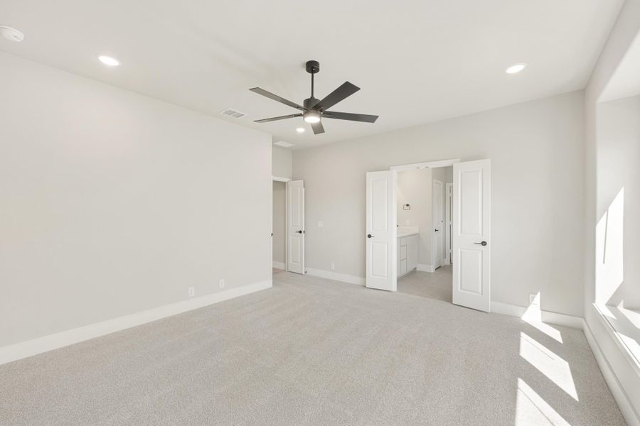 Empty bedroom with gray carpet, ceiling fan, and open doors leading to ensuite bathroom