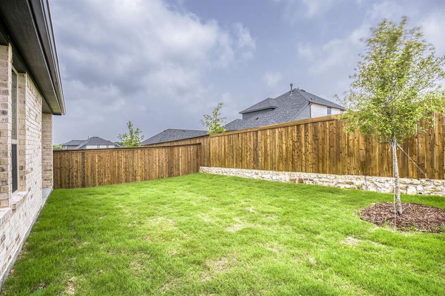 Expansive backyard featuring a lush lawn, privacy fencing, and a decorative stone retaining wall