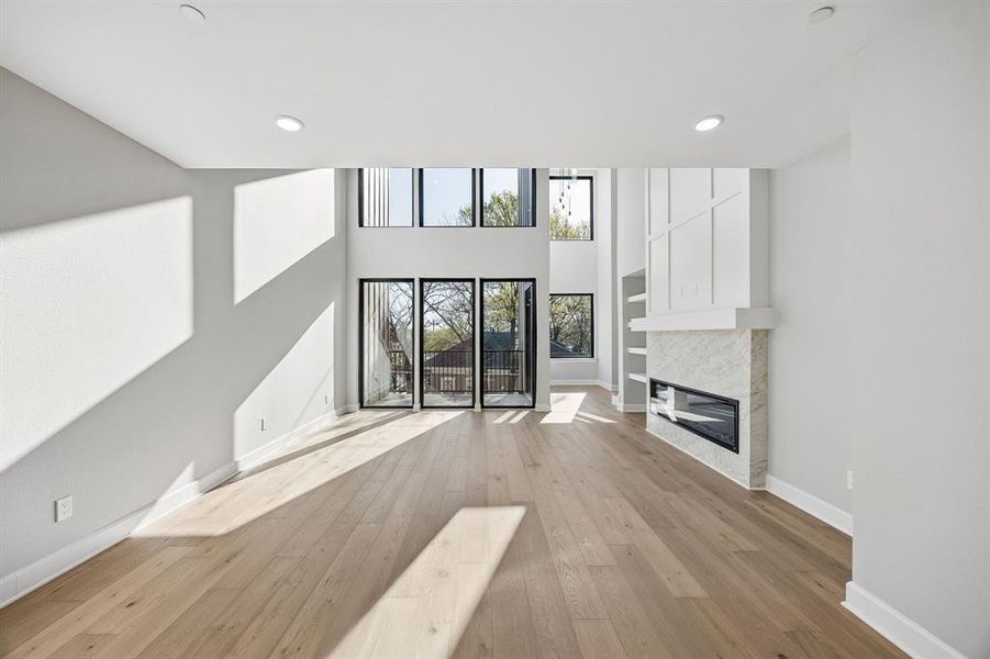 Unfurnished living room featuring light wood-type flooring, a tiled fireplace, a high ceiling, and recessed lighting Unfurnished living room featuring light wood-type flooring, a tiled fireplace, a high ceiling, and recessed lighting