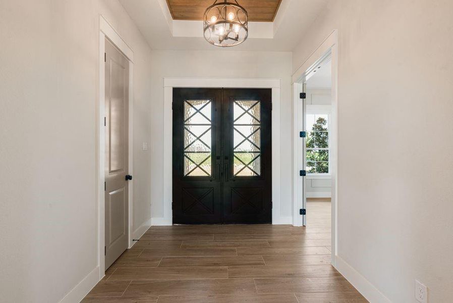 Foyer entrance with wood finish floors, hanging lights, and a raised ceiling