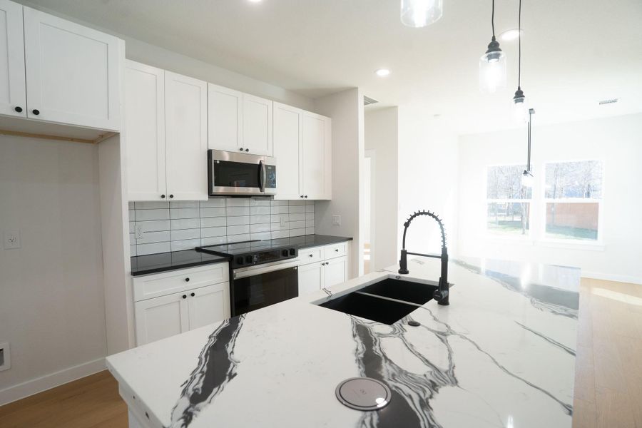 Kitchen with decorative light fixtures, white cabinetry, decorative backsplash, stainless steel microwave, and black electric range oven