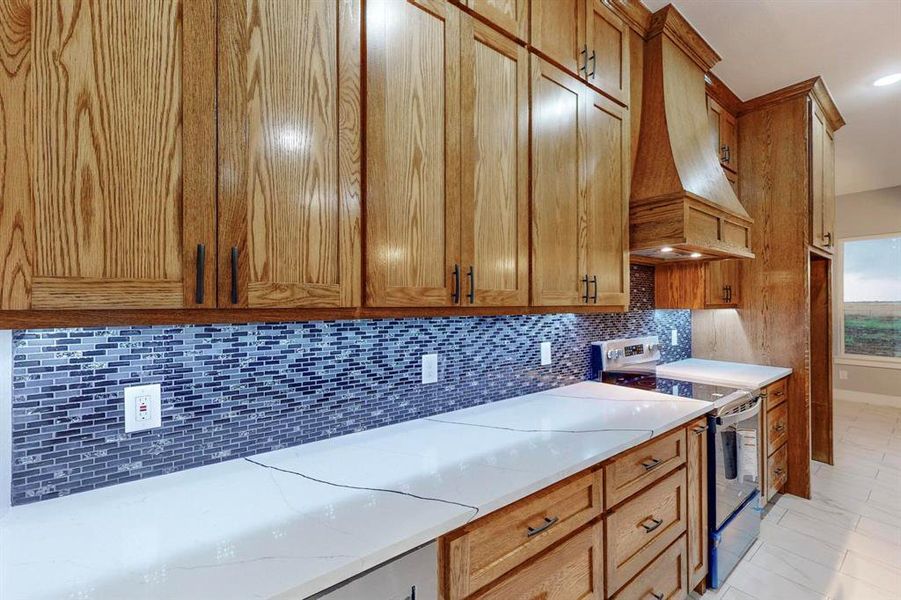 Kitchen featuring tasteful backsplash, light stone counters, light tile patterned flooring, custom range hood, and electric range