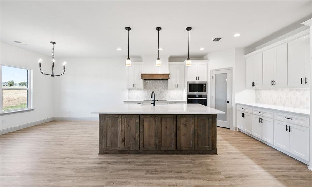 Kitchen featuring tasteful backsplash, pendant lighting, white cabinetry, dark brown cabinetry, and a center island with sink