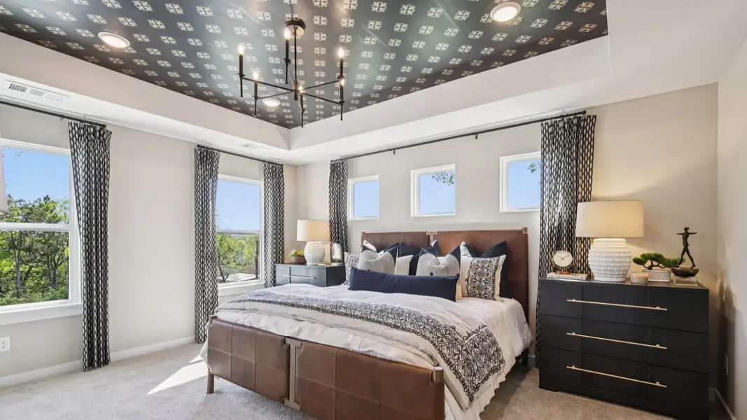 Large primary bedroom with accent tray ceiling and multiple windows for natural light