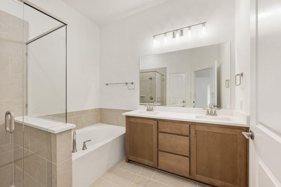 Bathroom with double sink vanity, soaking tub, and glass walk-in shower with tile surround