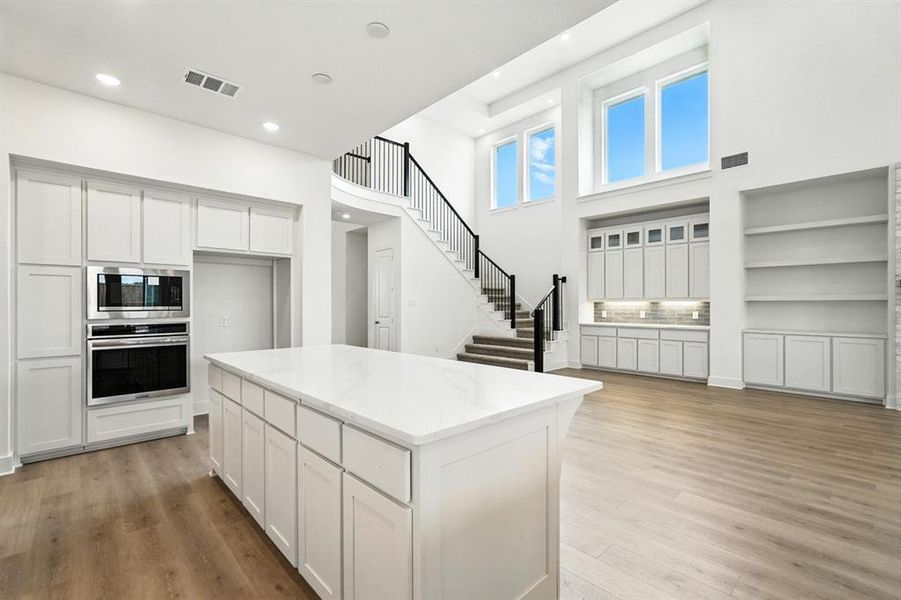 Kitchen with white cabinetry, a center island, appliances with stainless steel finishes, light wood-style floors, and light stone countertops Kitchen with white cabinetry, a center island, appliances with stainless steel finishes, light wood-style floors, and light stone countertops