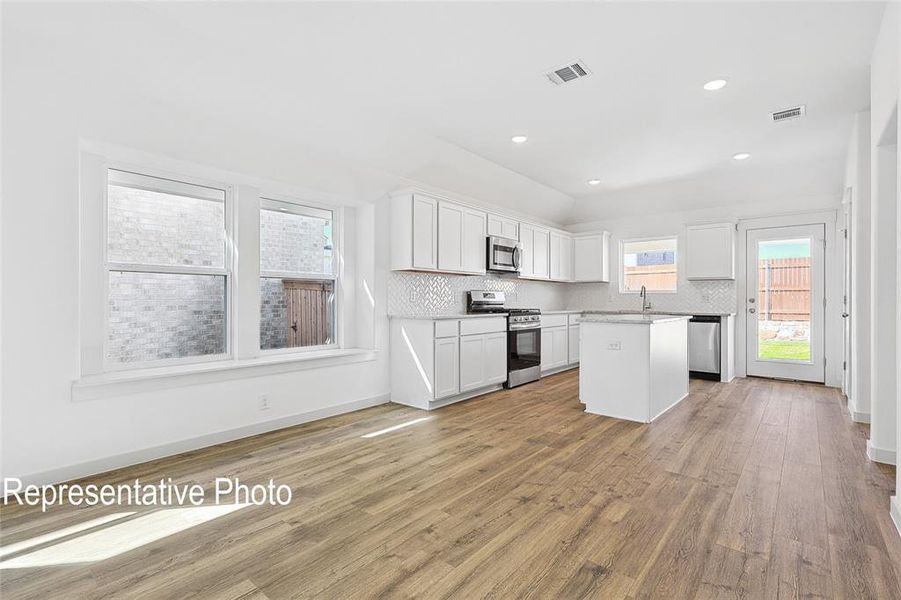 Kitchen with a kitchen island, white cabinets, decorative backsplash, light hardwood / wood-style floors, and stainless steel appliances