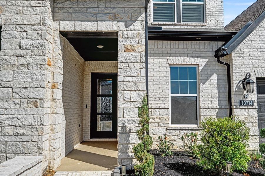 The recessed entry features floor-to-ceiling stone and a modern glass-panel door. Black hardware and contemporary lighting create a sophisticated first impression.