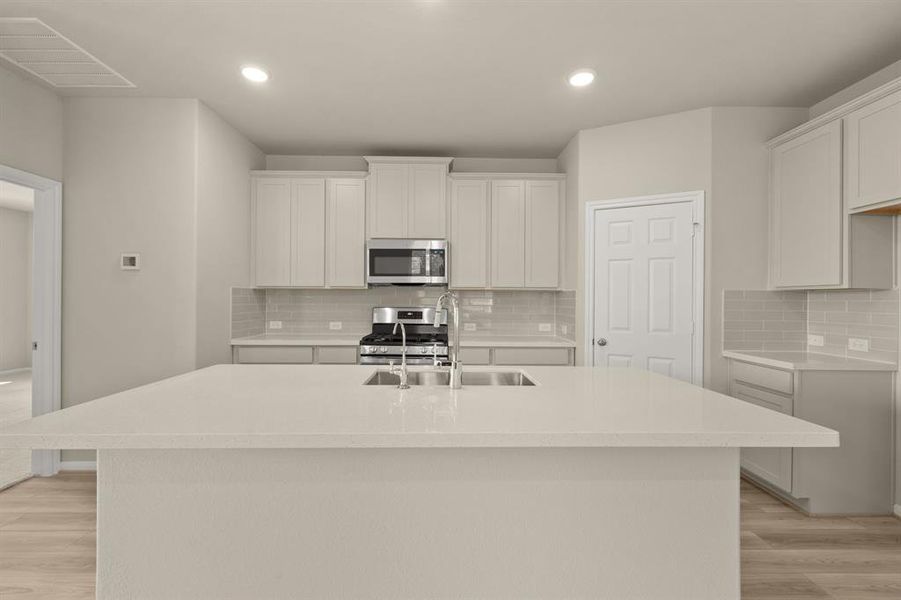 This light and bright kitchen features a large quartz island, white cabinets, a large sink overlooking your family room, recessed lighting, and beautiful backsplash.