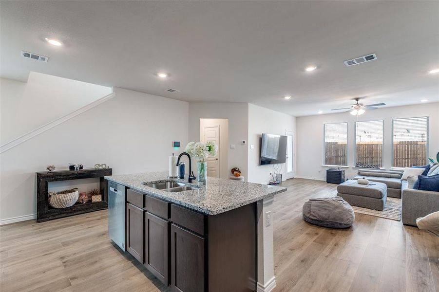 Kitchen with dark brown cabinets, light stone countertops, light wood-type flooring, recessed lighting, and an island with sink Kitchen with dark brown cabinets, light stone countertops, light wood-type flooring, recessed lighting, and an island with sink