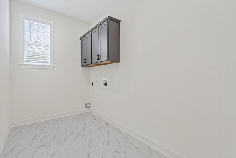 Laundry area featuring ceramic tile flooring, a window with blinds, and dark gray upper cabinetry with black hardware