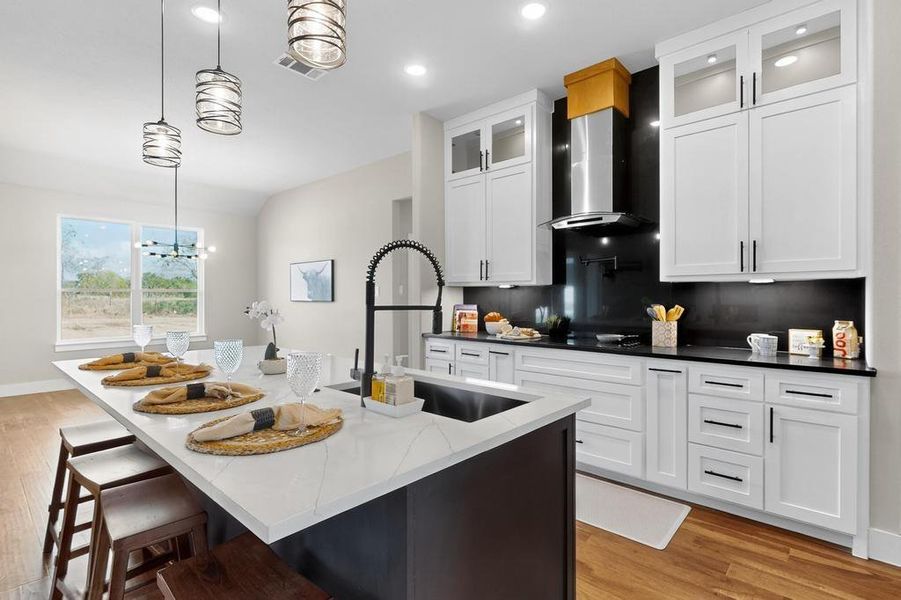 Kitchen featuring wall chimney range hood, light wood finished floors, pendant lighting, white cabinetry, and lofted ceiling