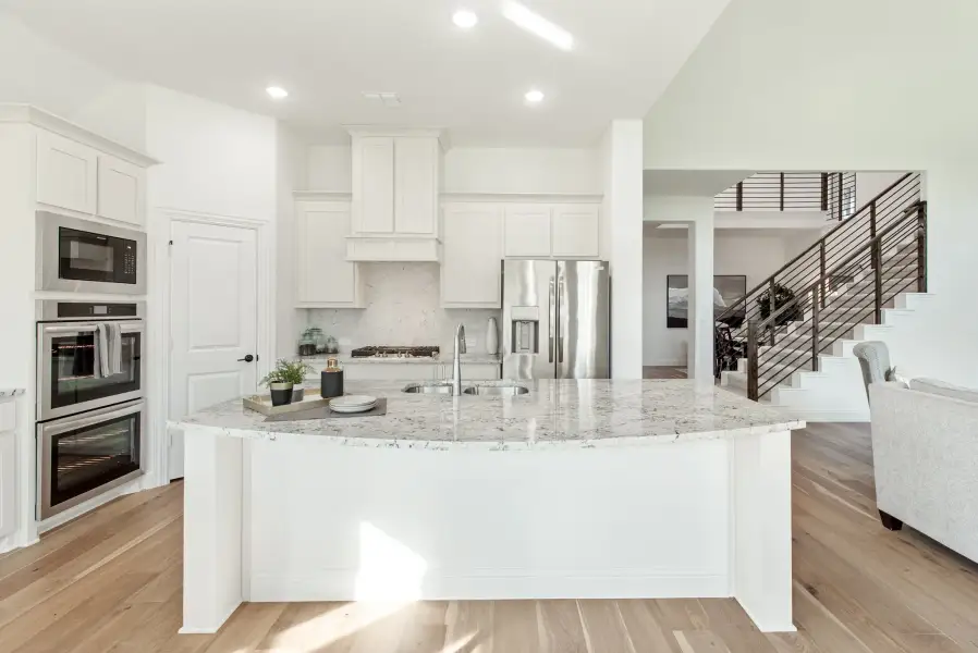Open kitchen with white cabinets, large granite island, stainless steel appliances, and hardwood floors