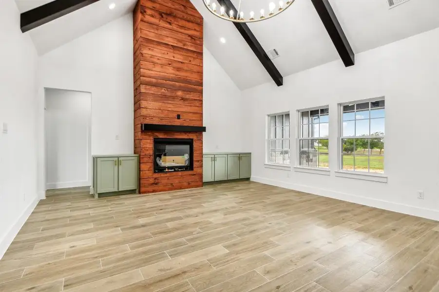 Unfurnished living room with beam ceiling, high vaulted ceiling, light wood-style floors, a chandelier, and a fireplace Unfurnished living room with beam ceiling, high vaulted ceiling, light wood-style floors, a chandelier, and a fireplace