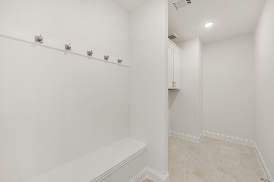 Mudroom with wall-mounted coat hooks, built-in bench, white upper cabinets, and tile flooring