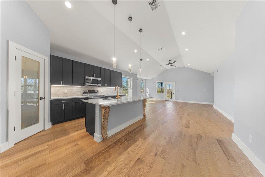 Kitchen with decorative light fixtures, dark cabinets, open floor plan, lofted ceiling, and an island with sink Kitchen with decorative light fixtures, dark cabinets, open floor plan, lofted ceiling, and an island with sink