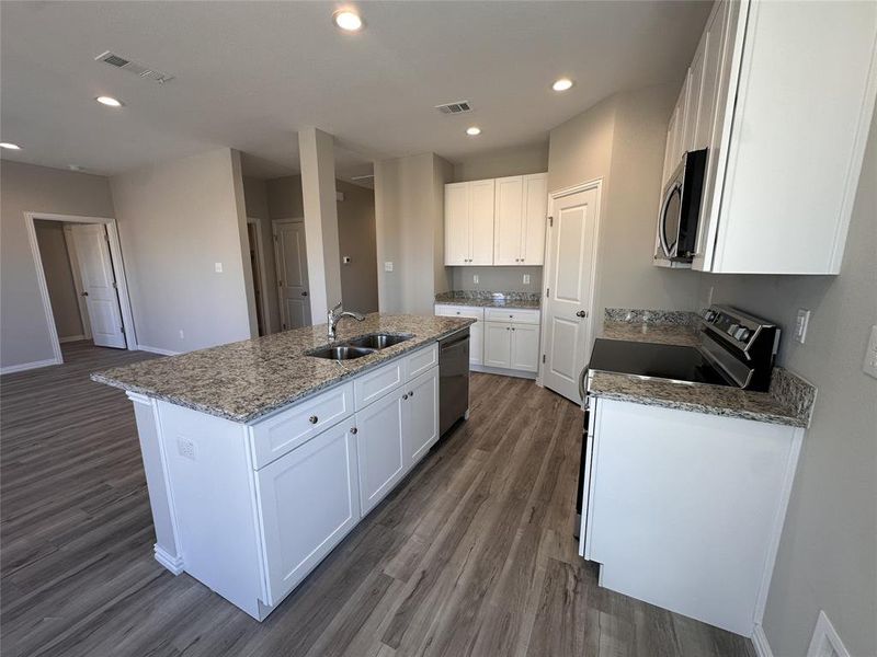 Kitchen with white cabinets, stainless steel appliances, a kitchen island with sink, and sink