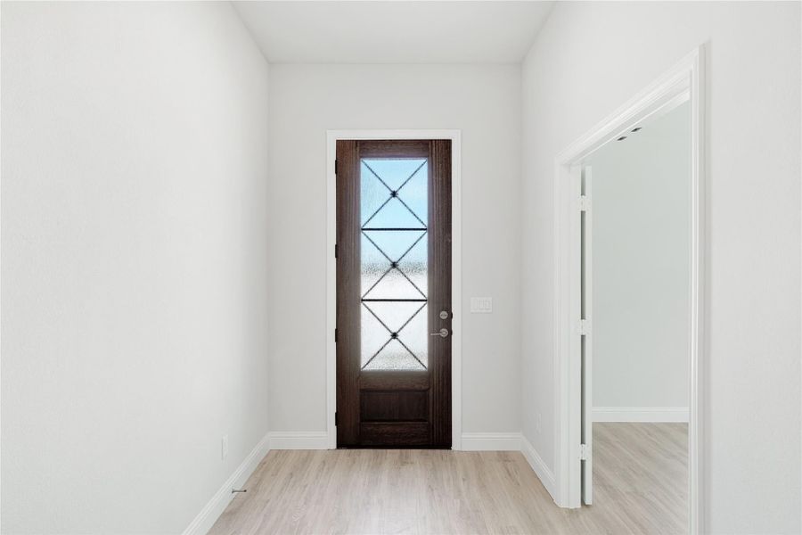 Entryway with dark wood front door featuring decorative glass panels and light hardwood floors Entryway with dark wood front door featuring decorative glass panels and light hardwood floors