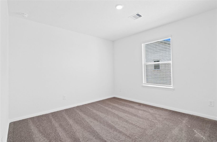 This secondary bedroom offers comfort and style with plush carpeting, neutral paint tones, recessed lighting, a large window with blinds, and a walk-in closet.