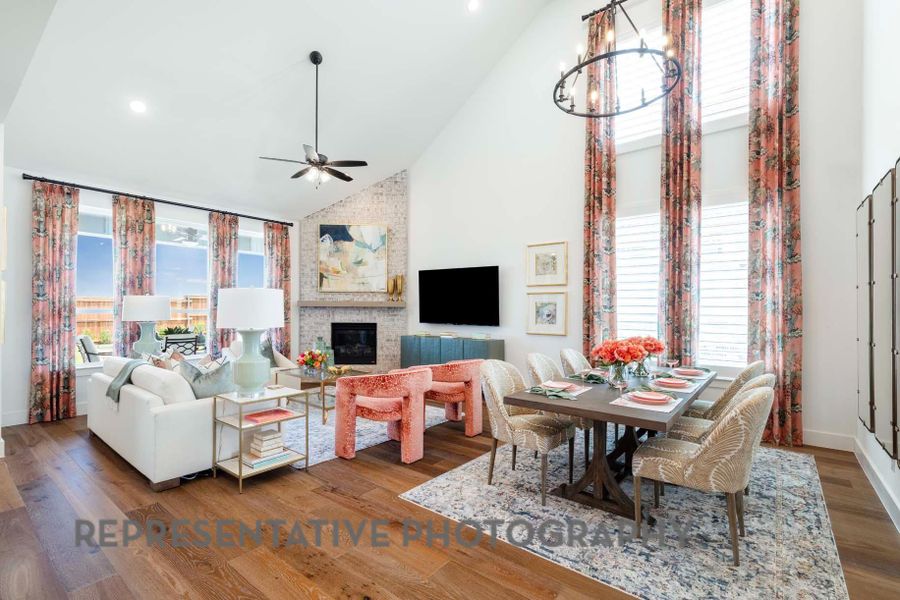 Living area featuring high vaulted ceiling, a large fireplace, baseboards, wood finished floors, and ceiling fan with notable chandelier Living area featuring high vaulted ceiling, a large fireplace, baseboards, wood finished floors, and ceiling fan with notable chandelier