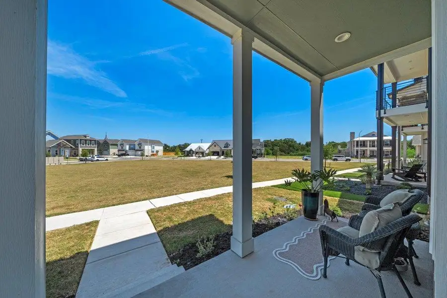 A sheltered concrete porch looks out across a paved sidewalk to a grassy neighborhood common area. A sheltered concrete porch looks out across a paved sidewalk to a grassy neighborhood common area.