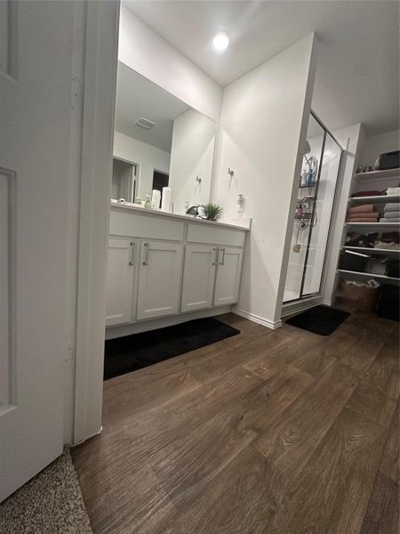 Full bath featuring double vanity, a stall shower, and dark wood-style flooring