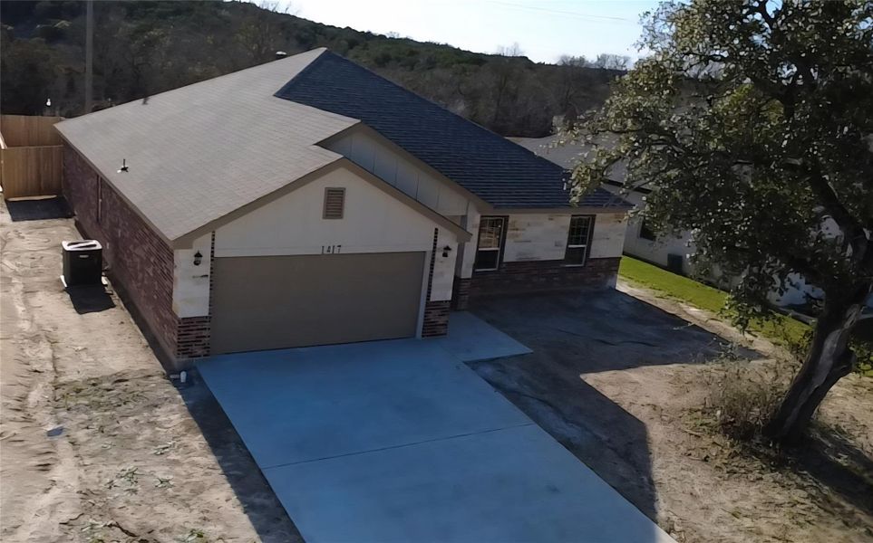 View of front facade with brick siding, concrete driveway, an attached garage, and a shingled roof