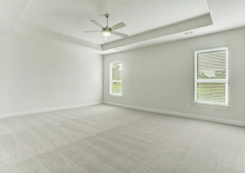 The master suite has light carpet, white walls and a ceiling fan.