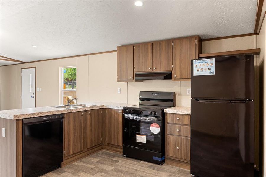 Kitchen featuring wood-finish cabinetry, light-toned countertops, and dark appliance suite
