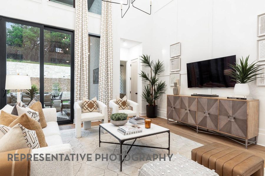 Living room featuring wood finished floors, a towering ceiling, baseboards, and a chandelier Living room featuring wood finished floors, a towering ceiling, baseboards, and a chandelier