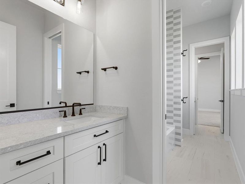 Bathroom vanity featuring a light-colored countertop, white cabinetry with dark hardware, and a large mirror