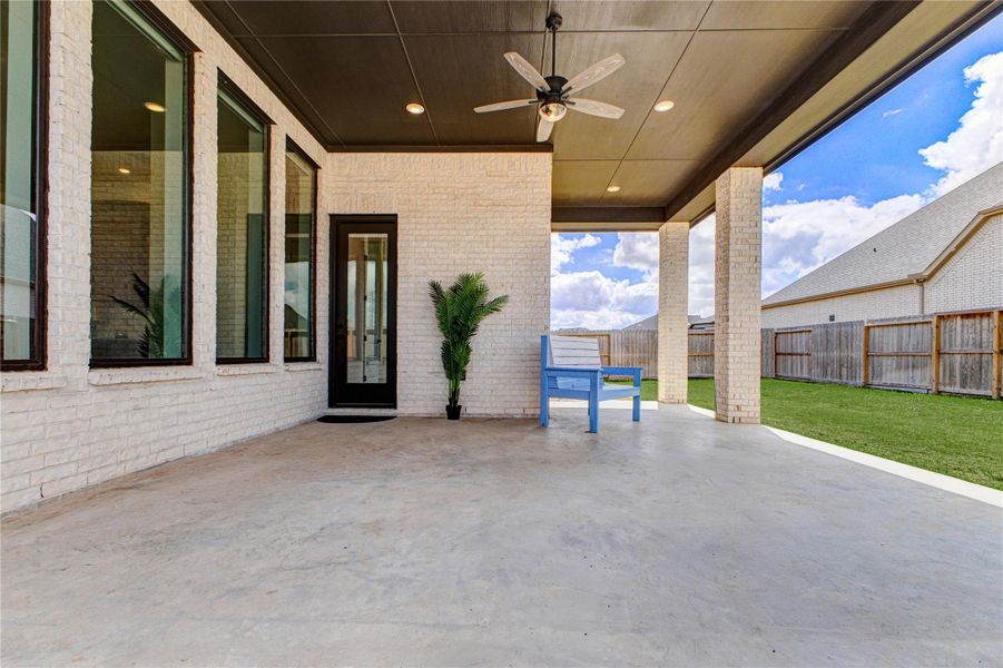 This photo showcases a spacious covered patio with a ceiling fan, large windows, and a door leading inside. The area features a simple potted plant and a blue bench, overlooking a well-kept lawn, perfect for outdoor relaxation. This photo showcases a spacious covered patio with a ceiling fan, large windows, and a door leading inside. The area features a simple potted plant and a blue bench, overlooking a well-kept lawn, perfect for outdoor relaxation.