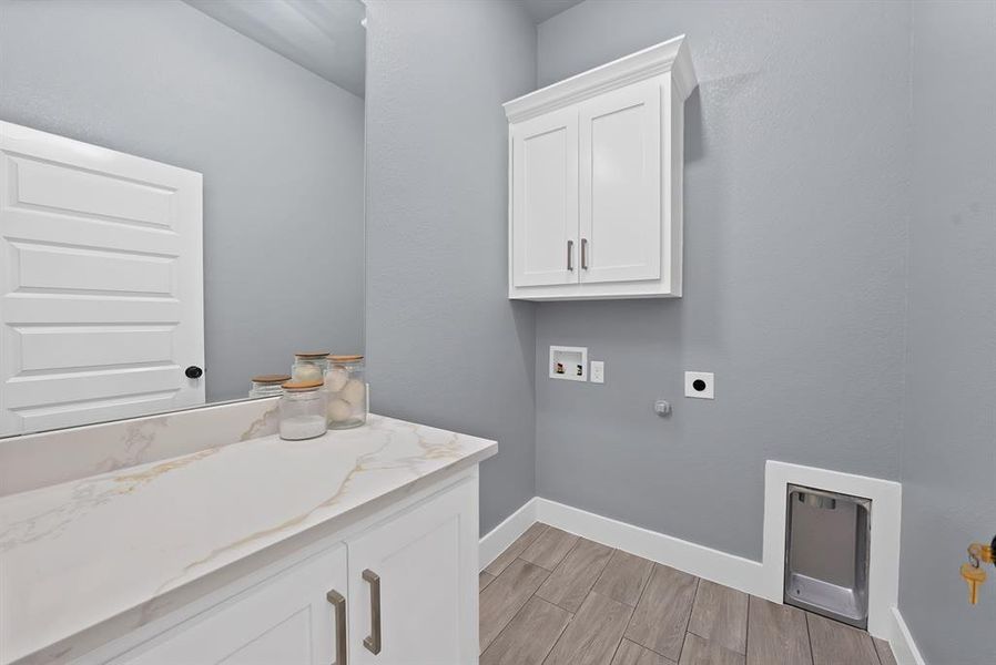 Laundry space featuring wood-finish flooring, a white paneled door, a built-in wall cabinet with brushed nickel hardware, and a countertop with integrated sink