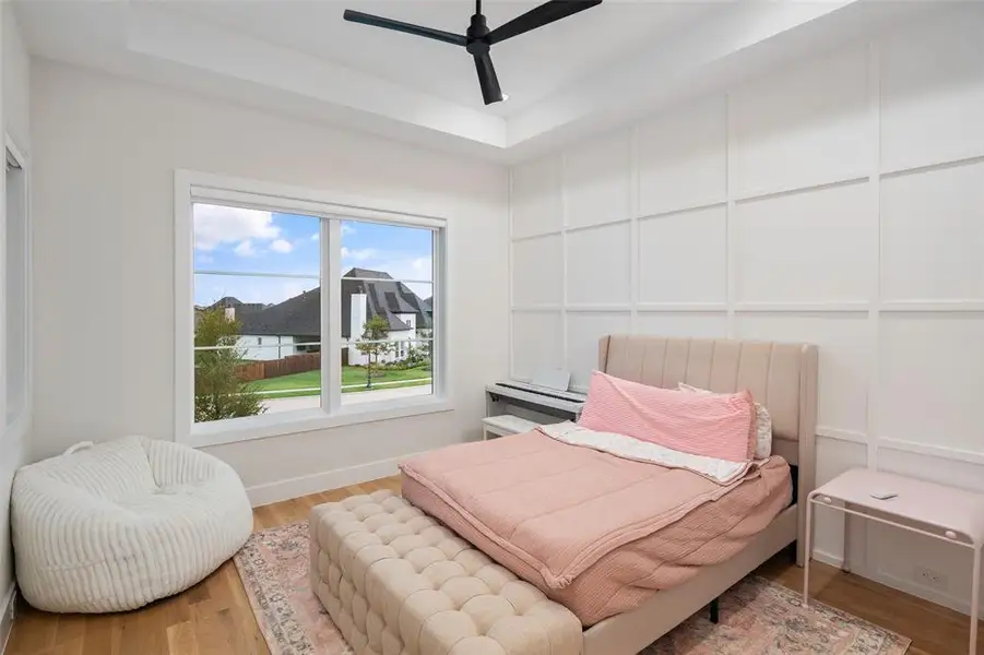 Secondary bedroom on the second floor featuring a large window that fills the space with natural light, a stylish accent wall, and an elegant tray ceiling that adds architectural interest. Remote-controlled shades provide both convenience and privacy, creating a comfortable and thoughtfully designed retreat.