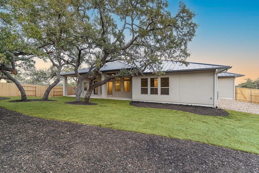 Back of property at dusk with a standing seam roof, a fenced backyard, a metal roof, and stucco siding Back of property at dusk with a standing seam roof, a fenced backyard, a metal roof, and stucco siding