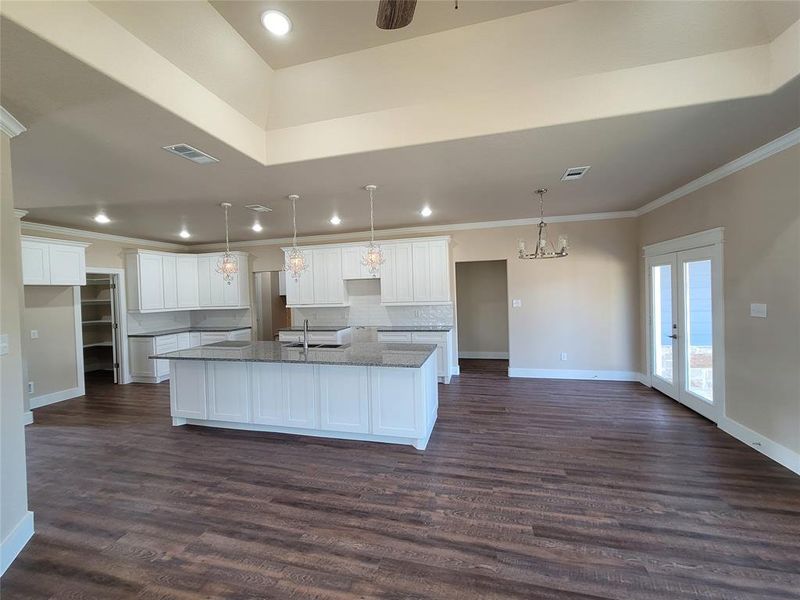 Kitchen with white cabinets, dark hardwood / wood-style flooring, dark stone countertops, and a center island with sink