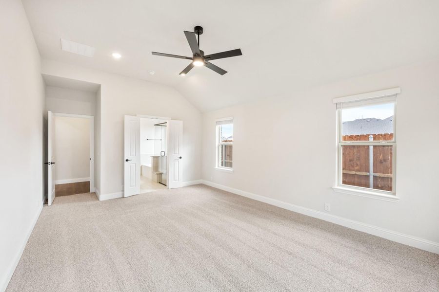 Empty bedroom with vaulted ceiling, ceiling fan, carpet flooring, and walk-in closet entrance Empty bedroom with vaulted ceiling, ceiling fan, carpet flooring, and walk-in closet entrance