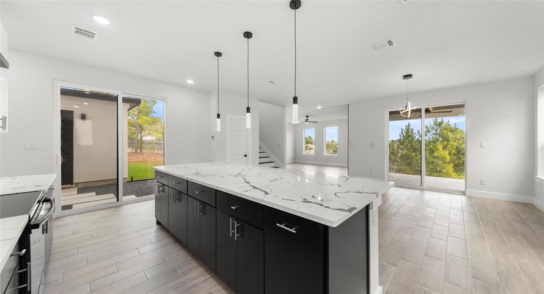Kitchen with dark cabinets, wood finish floors, light stone counters, and recessed lighting