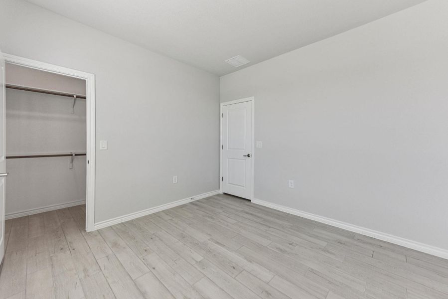 Unfurnished bedroom with a spacious closet and light wood-style flooring Unfurnished bedroom with a spacious closet and light wood-style flooring