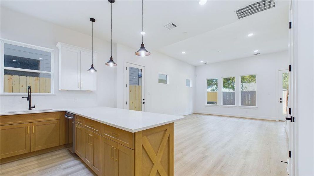 View of the first-floor living area from the kitchen. The natural wood cabinetry is thoughtfully complemented by white Calacatta quartz countertops and gold hardware. The 11-foot ceilings enhance the room's spacious feel, while three oversized windows fill the space with abundant natural light.