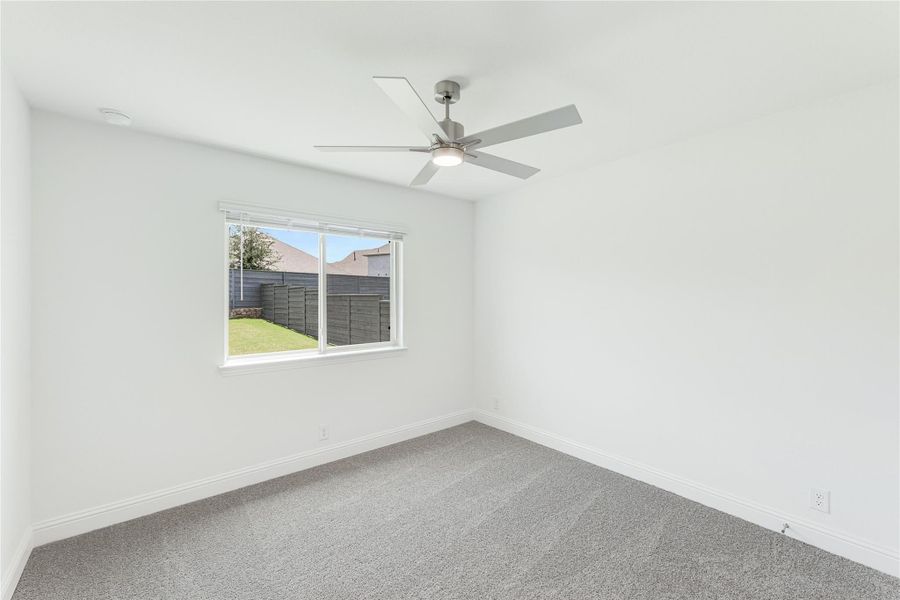 Empty bedroom with gray carpet, ceiling fan, and window overlooking backyard fence Empty bedroom with gray carpet, ceiling fan, and window overlooking backyard fence