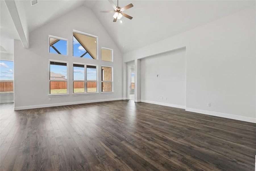 Unfurnished living room with dark wood finished floors, baseboards, high vaulted ceiling, and ceiling fan